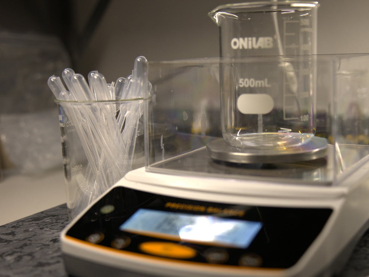 Glass beaker on a precision balance beside pipettes at the Petals & Smoke workbench.