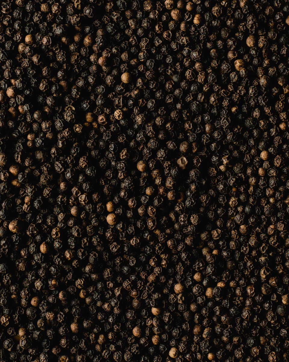 Close-up photograph of whole black peppercorns in warm light