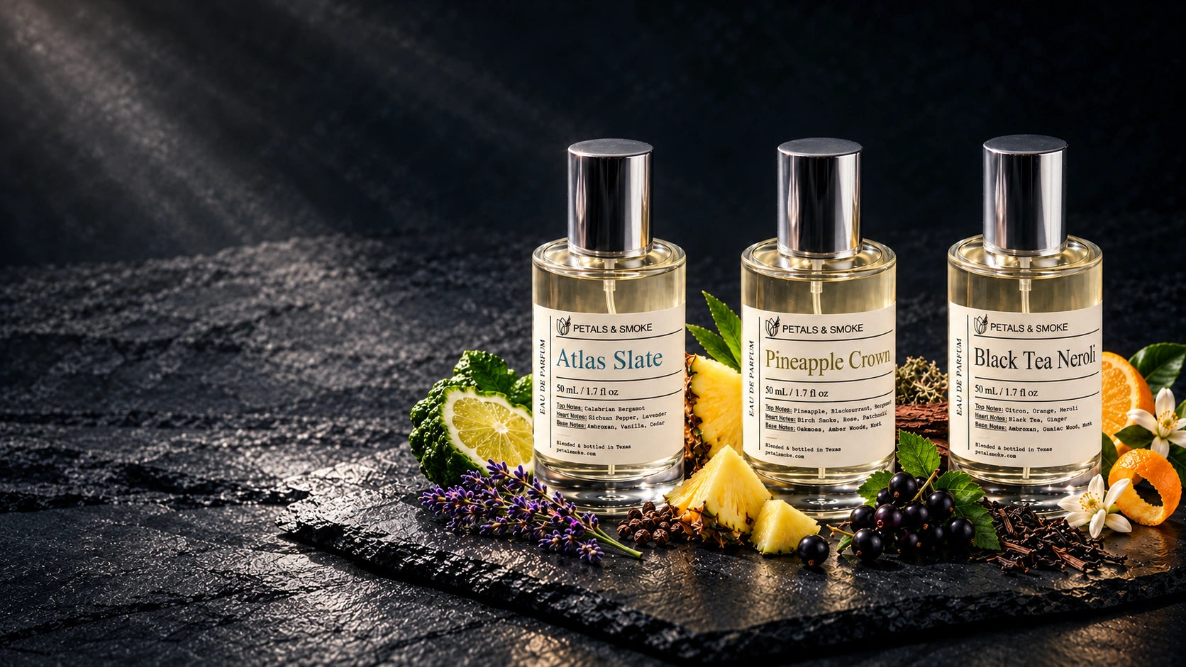 AI-enhanced product scene of Atlas Slate, Pineapple Crown and Black Tea Neroli 50 mL bottles on dark slate with citrus, pineapple, blackcurrant, lavender, tea and neroli.